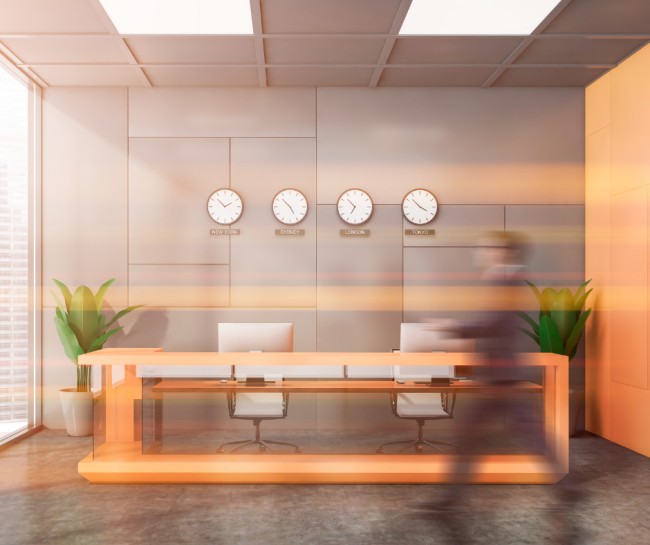 A photo of a desk with two spinning office chairs behind it. There is also a person in a suit walking in front of the desk.